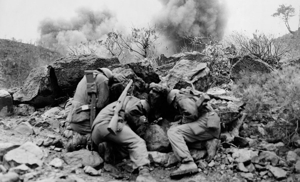 Korean Conflict. Men covering up behind rocks to shield themselves.